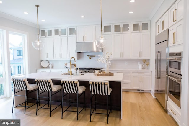 kitchen featuring light countertops, white cabinets, a kitchen island with sink, and under cabinet range hood