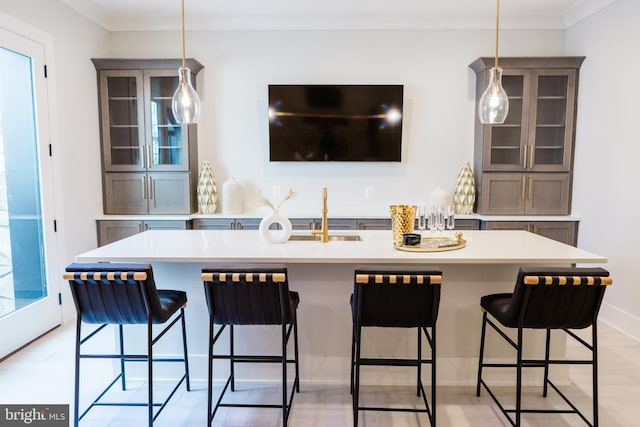 kitchen with glass insert cabinets, pendant lighting, a breakfast bar, light countertops, and a sink