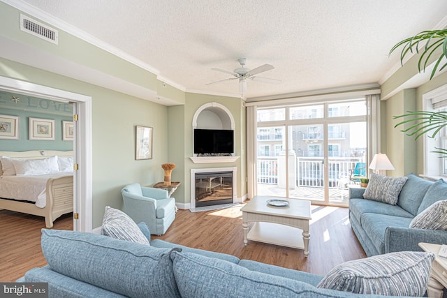 living room featuring crown molding, ceiling fan, light hardwood / wood-style floors, and a textured ceiling