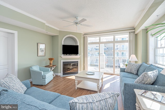 living room with ceiling fan, ornamental molding, light hardwood / wood-style flooring, and a textured ceiling