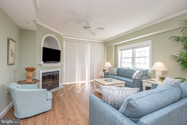 living room featuring ceiling fan, ornamental molding, light hardwood / wood-style floors, and a textured ceiling