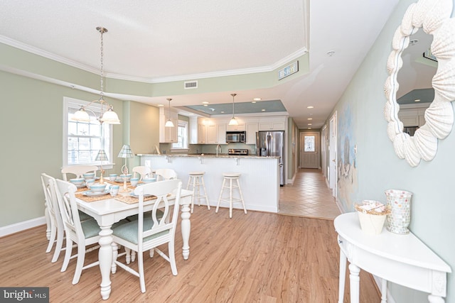 dining room featuring crown molding, sink, a raised ceiling, and light hardwood / wood-style floors