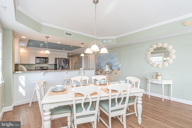 dining area featuring crown molding, a tray ceiling, a textured ceiling, and light wood-type flooring