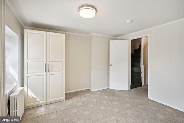 unfurnished bedroom with ornamental molding, radiator heating unit, light colored carpet, and a closet