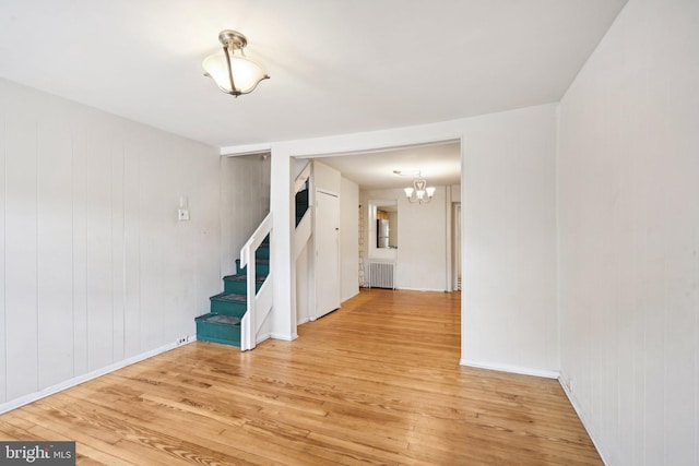 spare room with wood-type flooring, radiator heating unit, and an inviting chandelier