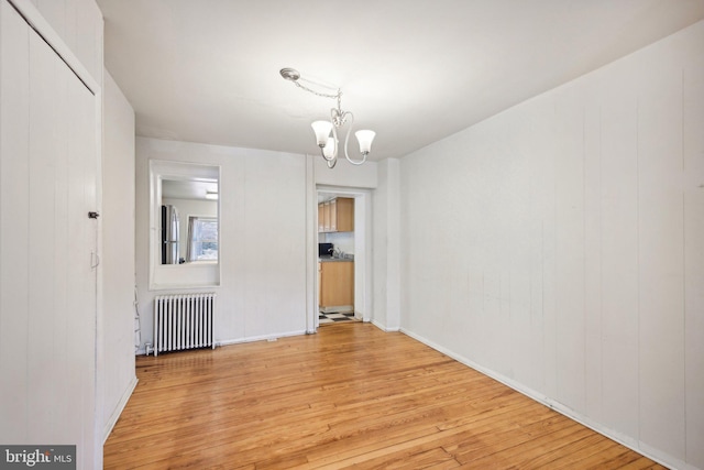 unfurnished dining area featuring an inviting chandelier, radiator heating unit, and light hardwood / wood-style floors