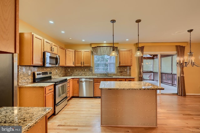 kitchen with light stone counters, tasteful backsplash, light wood-type flooring, pendant lighting, and stainless steel appliances