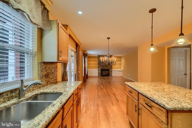 kitchen with sink, hanging light fixtures, light stone counters, a fireplace, and light wood-type flooring