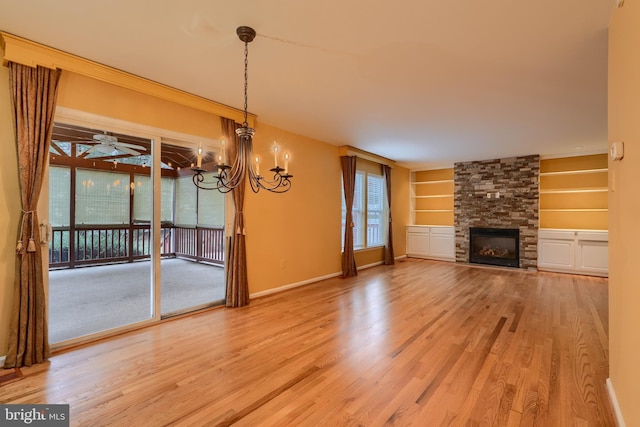 unfurnished living room featuring wood-type flooring, a stone fireplace, ceiling fan with notable chandelier, and built in features