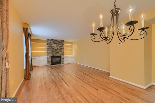 unfurnished living room featuring a stone fireplace, a chandelier, built in features, and light hardwood / wood-style floors