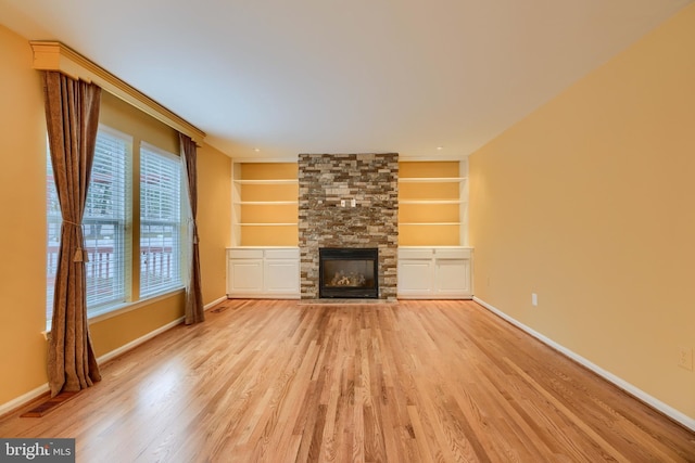 unfurnished living room with a stone fireplace, built in features, and light wood-type flooring