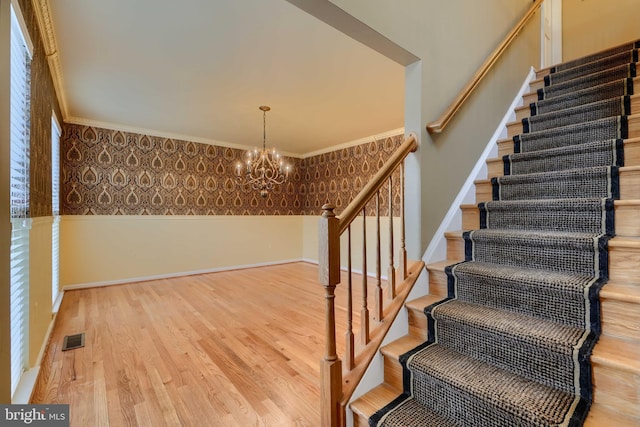 staircase with crown molding, a notable chandelier, and hardwood / wood-style flooring