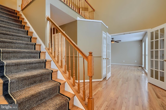 stairway featuring french doors, ceiling fan, hardwood / wood-style floors, and a high ceiling