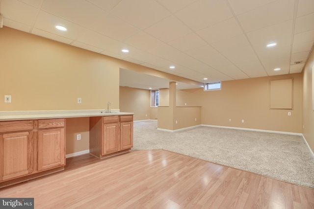 interior space with a drop ceiling, sink, and light hardwood / wood-style floors