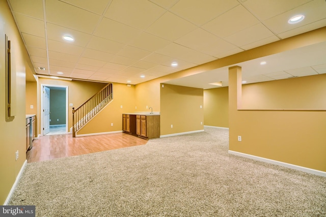 basement with a paneled ceiling, light colored carpet, and indoor wet bar