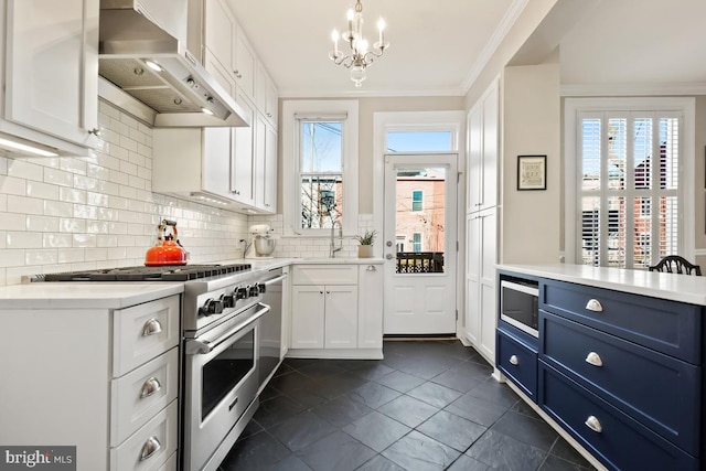 kitchen with blue cabinetry, wall chimney exhaust hood, appliances with stainless steel finishes, and light countertops