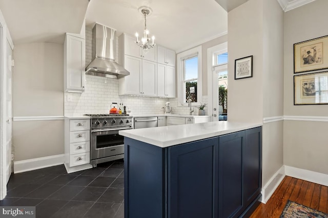 kitchen featuring stainless steel appliances, white cabinets, light countertops, decorative backsplash, and wall chimney exhaust hood