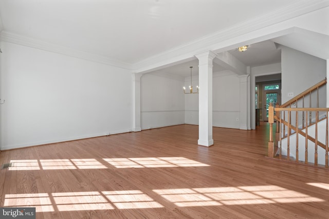 unfurnished living room featuring a chandelier, ornate columns, wood finished floors, crown molding, and stairway