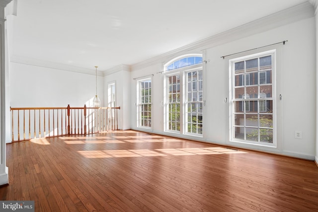 empty room featuring hardwood / wood-style flooring, crown molding, and a chandelier