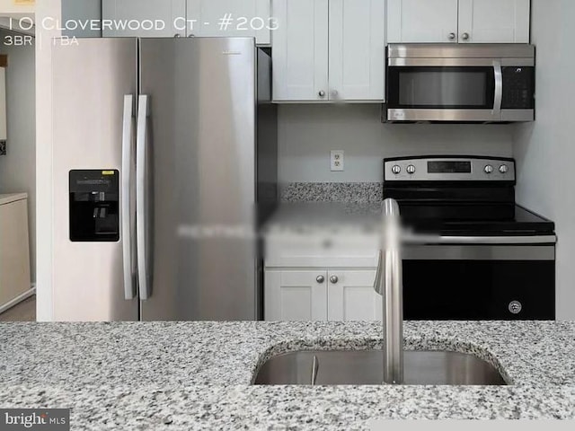 kitchen featuring stainless steel appliances, white cabinets, and light stone counters