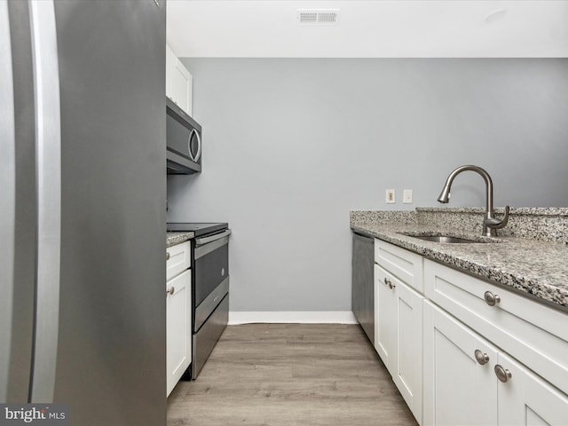 kitchen with appliances with stainless steel finishes, sink, white cabinets, and light stone counters