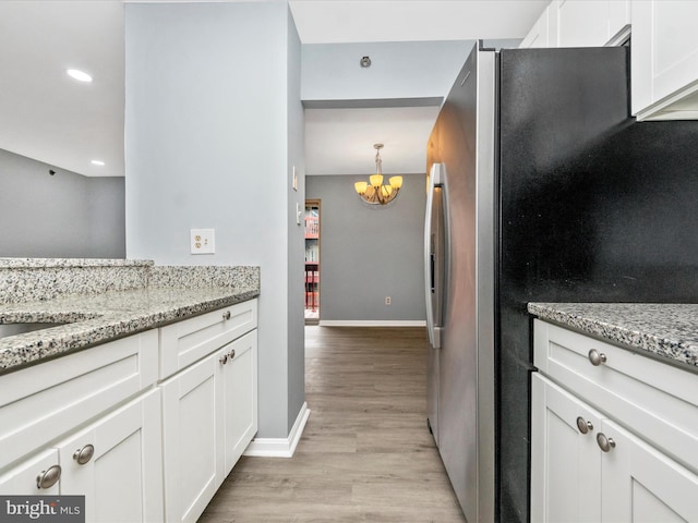 kitchen featuring pendant lighting, white cabinetry, stainless steel fridge, light hardwood / wood-style floors, and light stone countertops