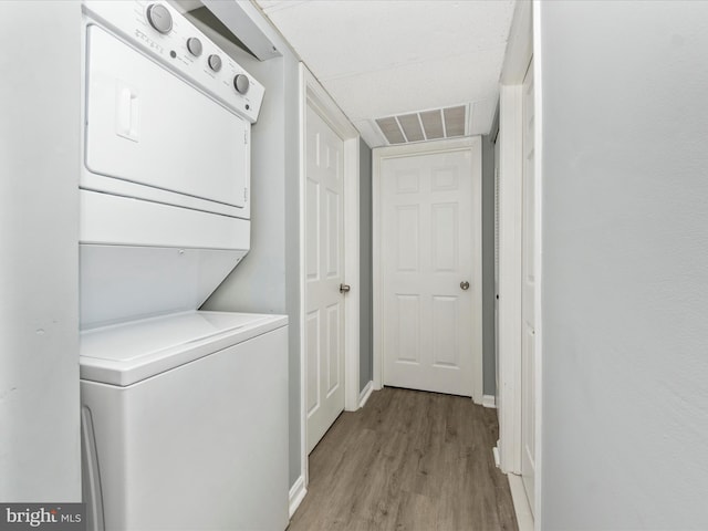 laundry area with stacked washer / drying machine and light hardwood / wood-style floors