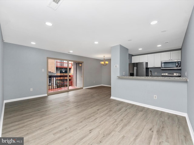 kitchen featuring appliances with stainless steel finishes, white cabinetry, an inviting chandelier, light hardwood / wood-style floors, and kitchen peninsula