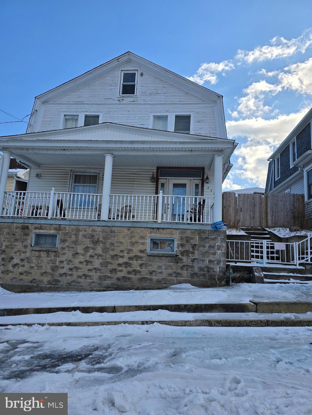 view of front of property with covered porch, a gambrel roof, and fence