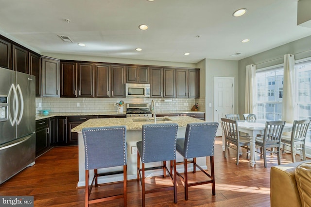 kitchen featuring sink, stainless steel appliances, an island with sink, and light stone countertops