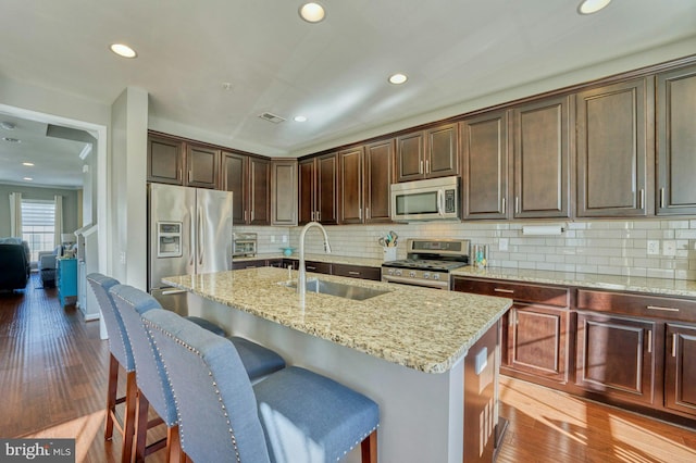 kitchen featuring light stone counters, sink, stainless steel appliances, and a center island with sink