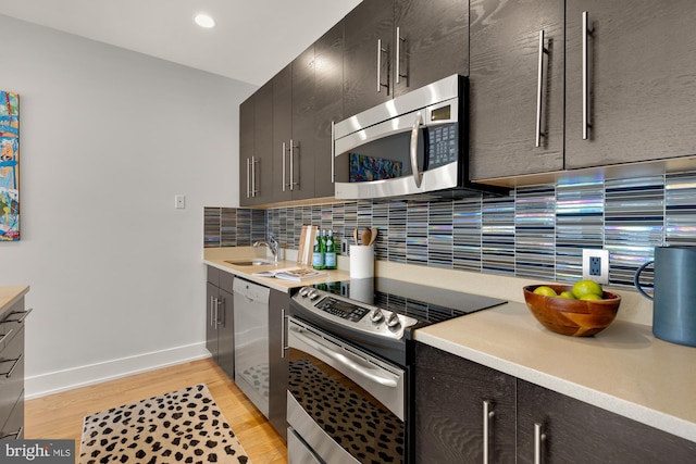 kitchen with light wood finished floors, light countertops, backsplash, appliances with stainless steel finishes, and a sink