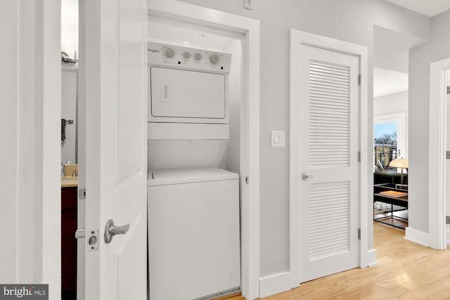 clothes washing area with laundry area, light wood finished floors, stacked washing maching and dryer, and baseboards