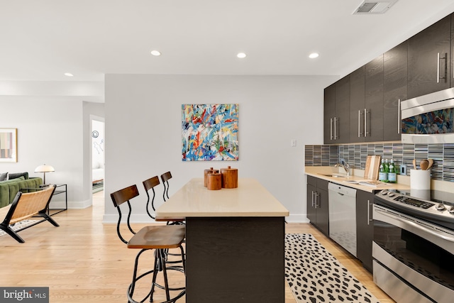 kitchen featuring tasteful backsplash, visible vents, appliances with stainless steel finishes, light countertops, and a kitchen bar