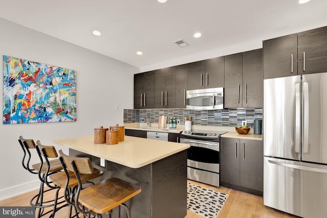 kitchen featuring appliances with stainless steel finishes, light countertops, light wood-style floors, a kitchen bar, and backsplash