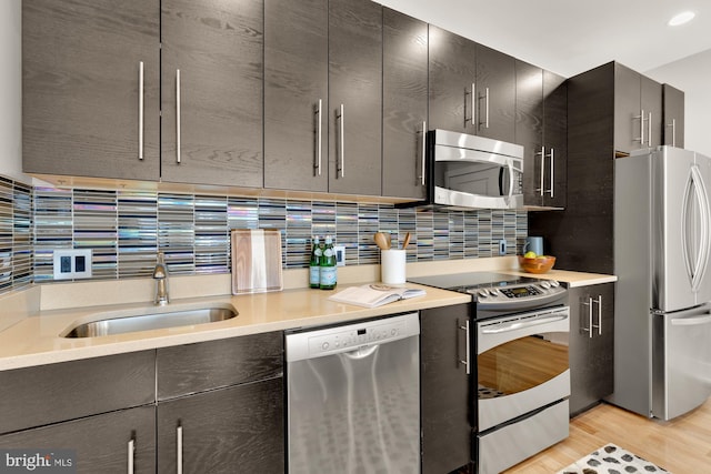 kitchen featuring tasteful backsplash, light countertops, appliances with stainless steel finishes, a sink, and light wood-type flooring