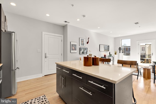 kitchen with a kitchen island, light countertops, dark cabinets, and freestanding refrigerator