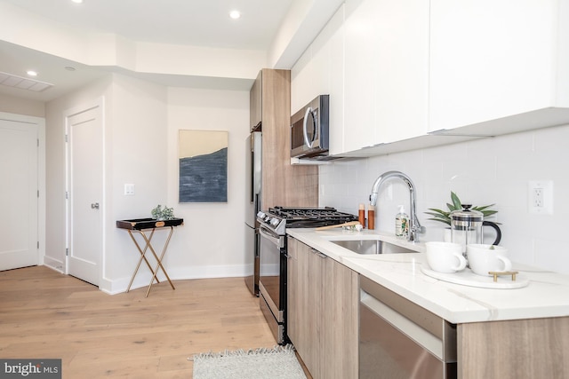 kitchen featuring appliances with stainless steel finishes, white cabinetry, sink, light stone counters, and light hardwood / wood-style flooring