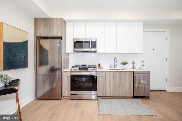 kitchen with white cabinetry, sink, decorative backsplash, stainless steel appliances, and light wood-type flooring