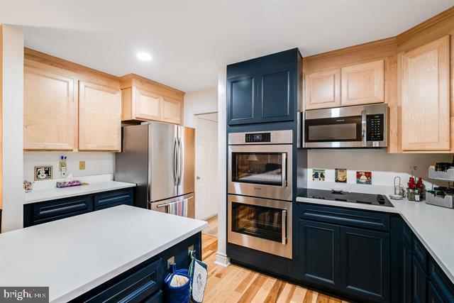 kitchen featuring stainless steel appliances, light brown cabinetry, light hardwood / wood-style floors, and blue cabinets