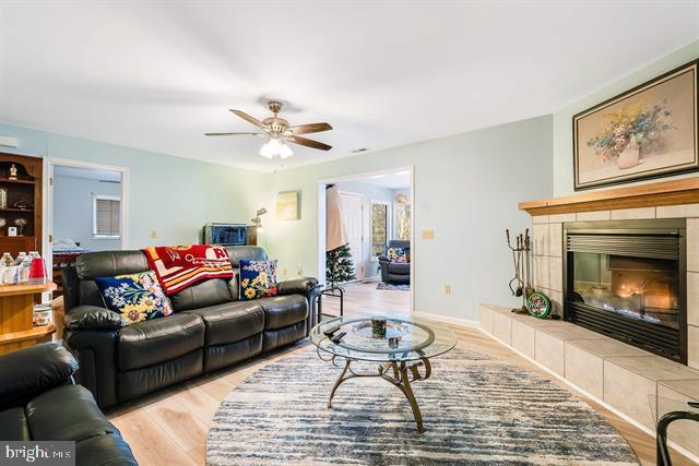 living room with ceiling fan, a tiled fireplace, and light wood-type flooring