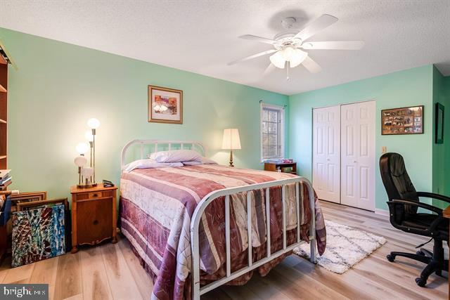 bedroom featuring ceiling fan, a closet, a textured ceiling, and light wood-type flooring