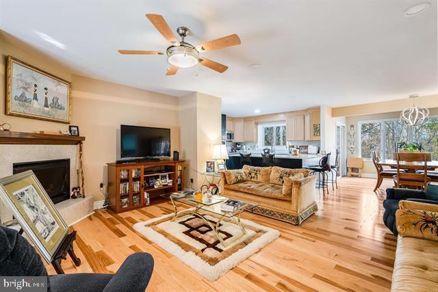 living room with a tiled fireplace, ceiling fan with notable chandelier, and light hardwood / wood-style flooring