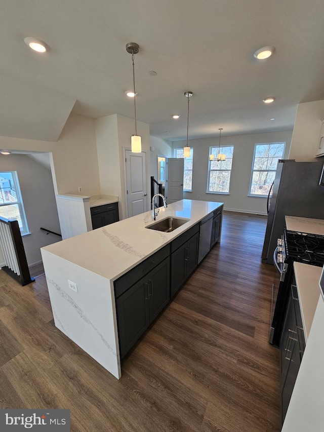 kitchen with decorative light fixtures, sink, stove, a kitchen island with sink, and dark wood-type flooring