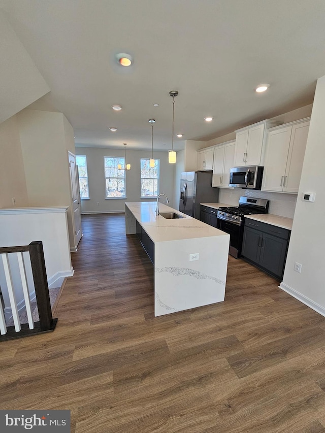 kitchen with pendant lighting, appliances with stainless steel finishes, white cabinetry, dark hardwood / wood-style floors, and an island with sink