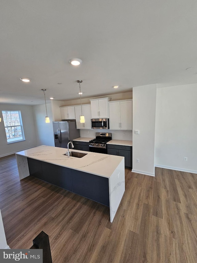 kitchen with appliances with stainless steel finishes, decorative light fixtures, white cabinetry, an island with sink, and sink