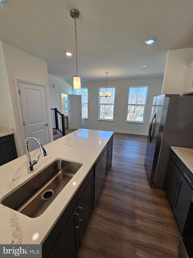 kitchen with dark wood-type flooring, sink, hanging light fixtures, stainless steel refrigerator, and white cabinets