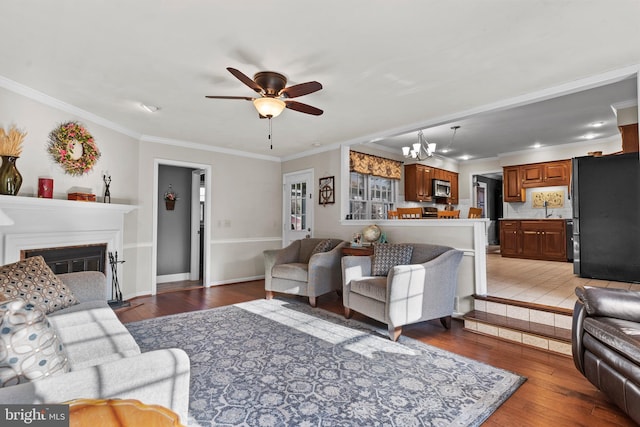 living room with ceiling fan with notable chandelier, ornamental molding, and light hardwood / wood-style floors