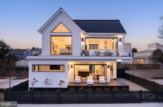 back of property at dusk with a standing seam roof, metal roof, a fenced front yard, and an outdoor living space