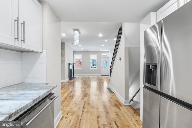 kitchen featuring appliances with stainless steel finishes, light stone counters, light hardwood / wood-style floors, backsplash, and white cabinetry